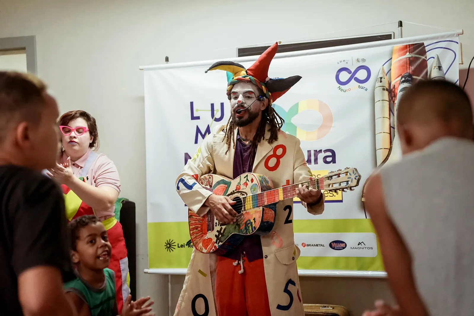 Artista com violão colorido se apresentando para crianças no LUMA Neurocultura
