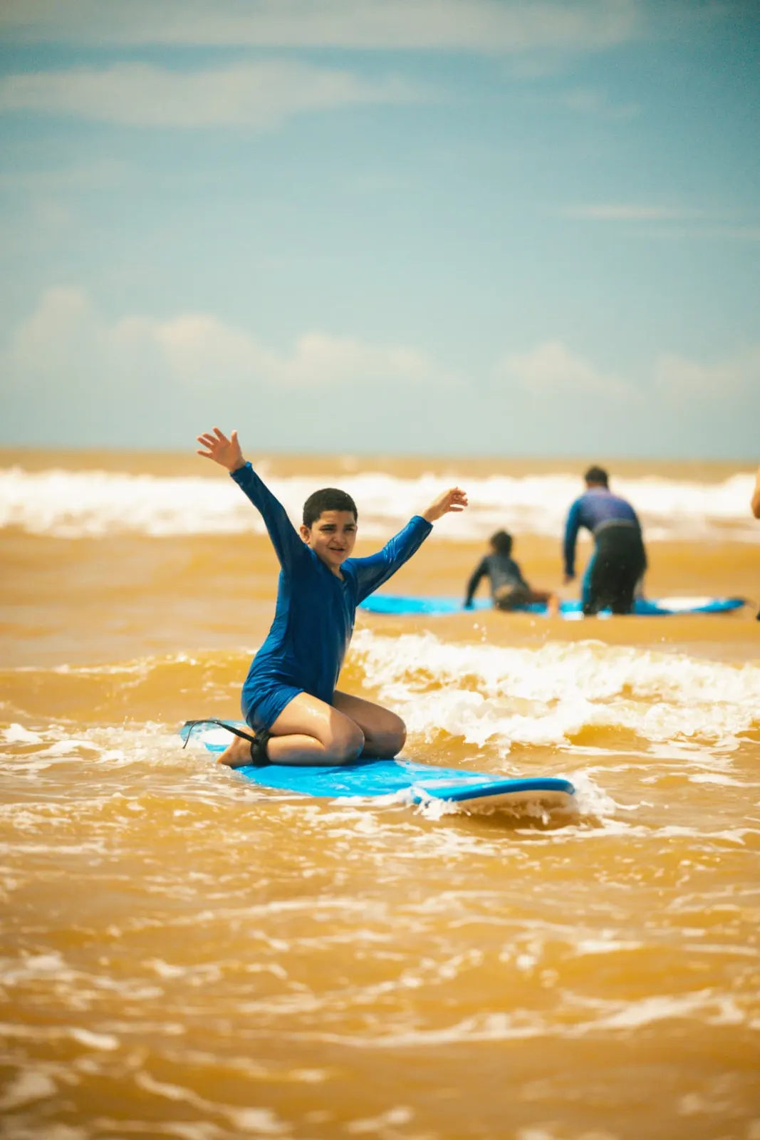 Criança comemorando de braços abertos sobre a prancha no mar