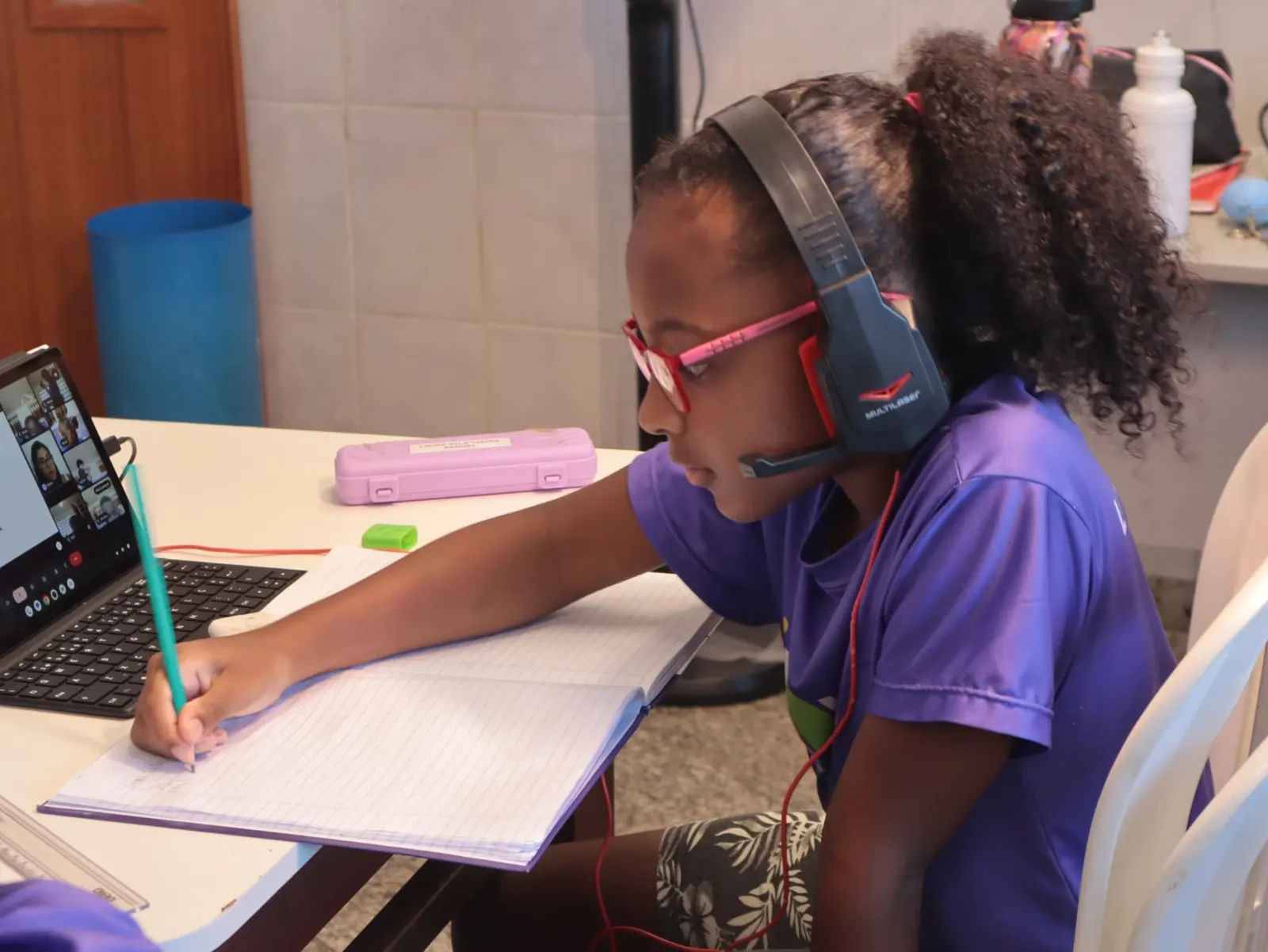 Aluna escrevendo no caderno durante aula online com tutoria ao vivo