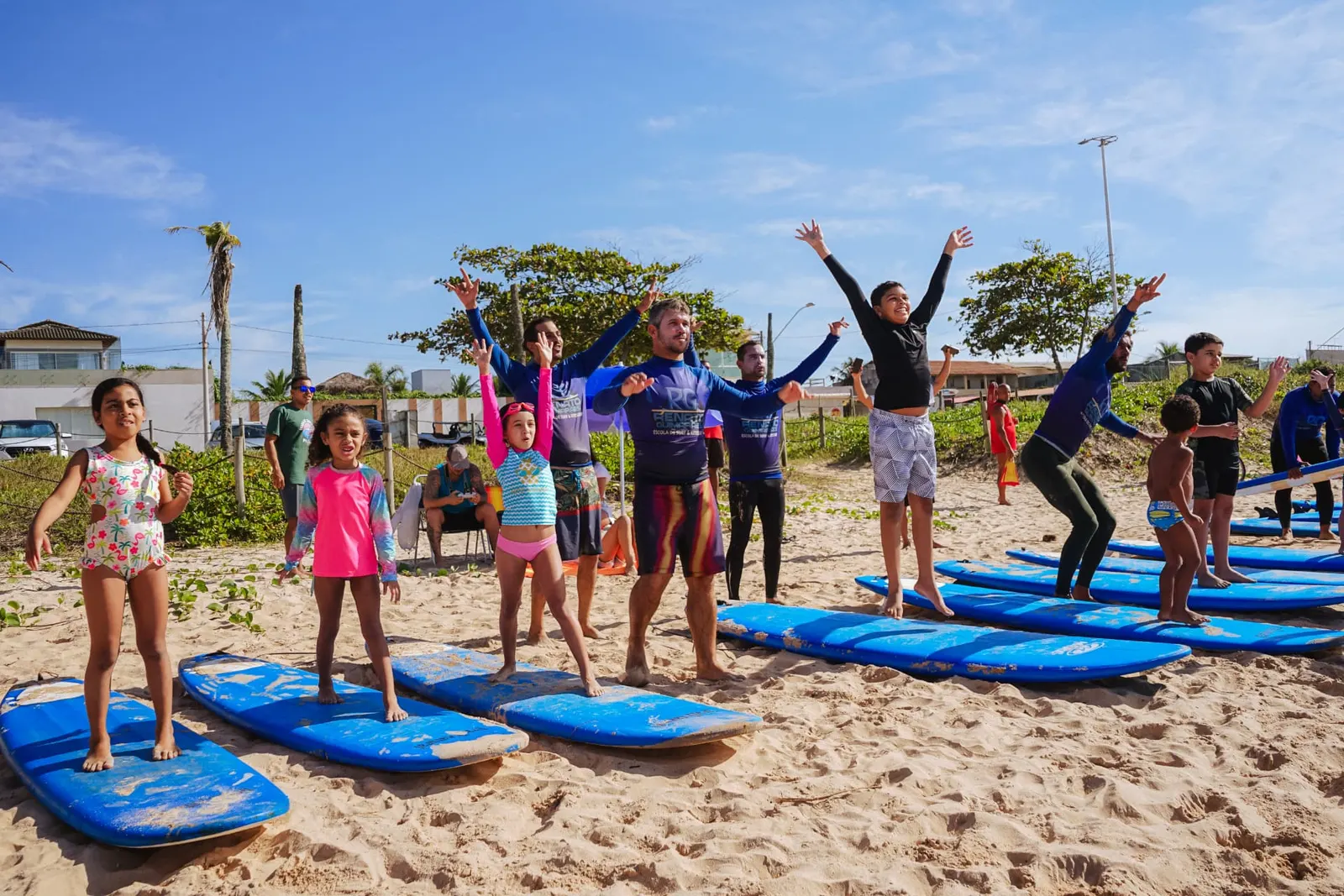 Crianças em pé nas pranchas durante aula de surfe adaptado na praia
